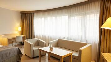 Una habitación de hotel con cama, sofá, mesita, escritorio y lámpara.