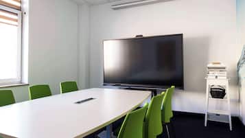 A conference room with a large flat-screen TV, a white table, and green chairs.