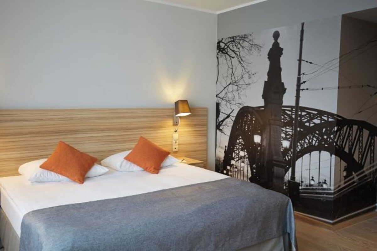 Hotelkamer met een bed, nachtkastje, lamp en een muurschildering van een brug.
