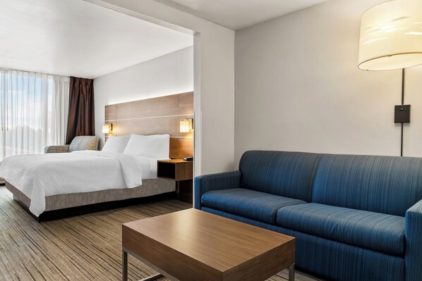 A hotel room with a bed, a sofa, a coffee table, and a lamp.