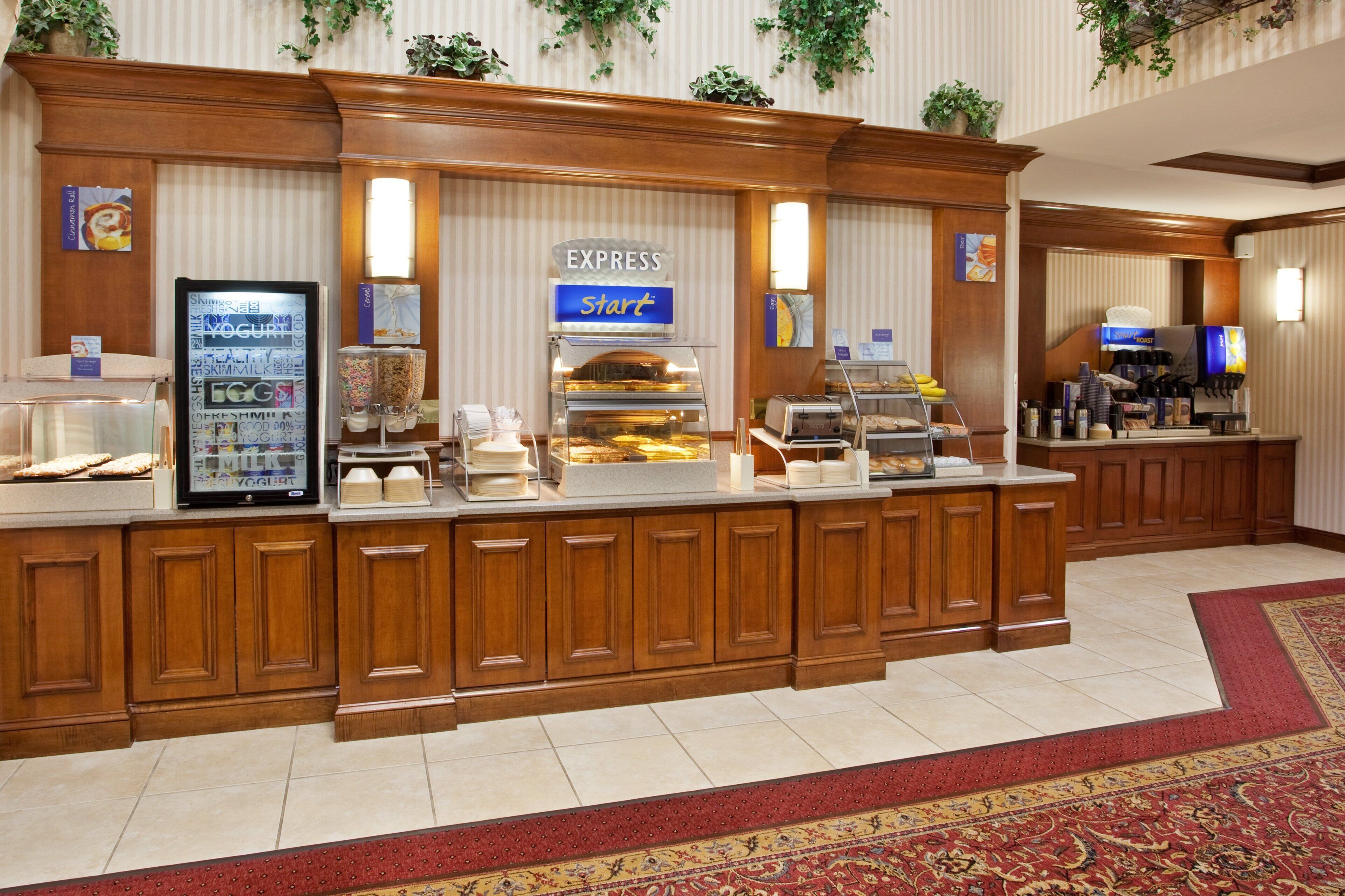 A hotel breakfast area with a self-serve station, including a yogurt dispenser, cereal, and a coffee machine.
