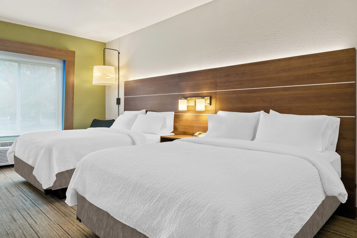 Habitación de hotel con dos camas, cabecero de madera, lámparas de noche y una ventana con persianas.