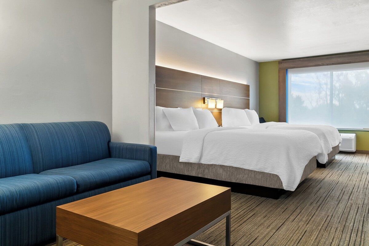 Habitación de hotel con cama, dos mesitas de noche, sofá y ventana con vistas a árboles.