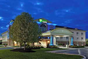 Un hotel Holiday Inn Express con entrada cubierta, un árbol grande en primer plano y un césped bien cuidado.