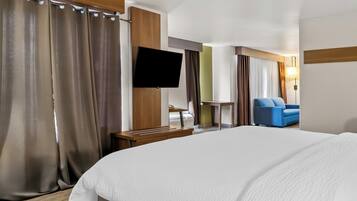 A hotel room with a large bed, a flat-screen TV mounted on the wall, a desk with a chair, and a blue sofa.