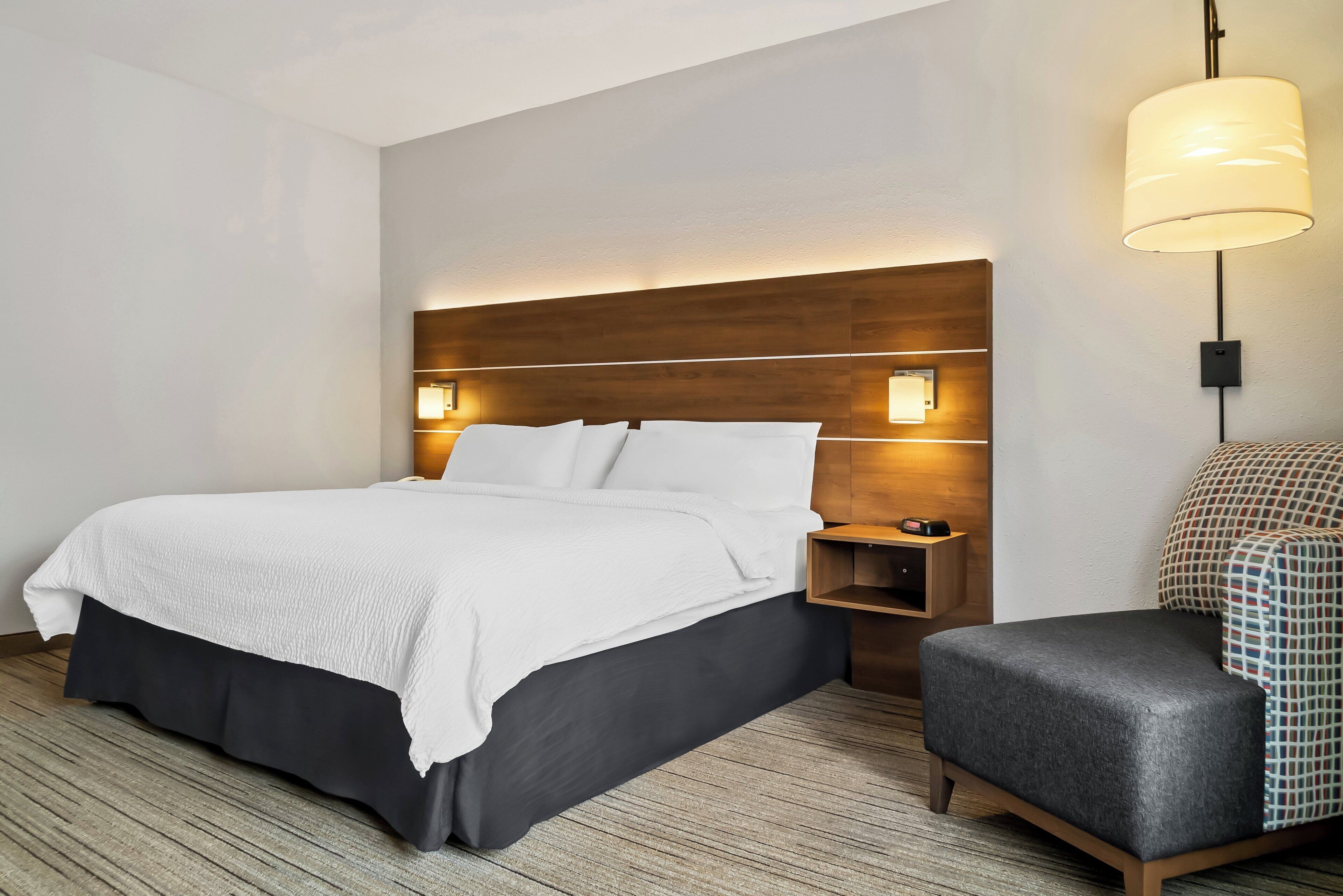 Habitación de hotel con una cama grande, mesitas de noche, una silla y una lámpara de pared.