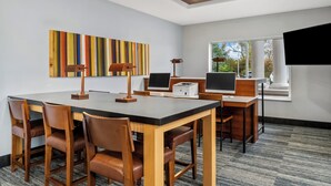 Een moderne vergaderruimte met een lange tafel, stoelen, een bureau, een computer en een beamer.