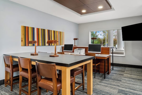 A modern meeting room with a long table, chairs, a desk, a computer, and a projector.