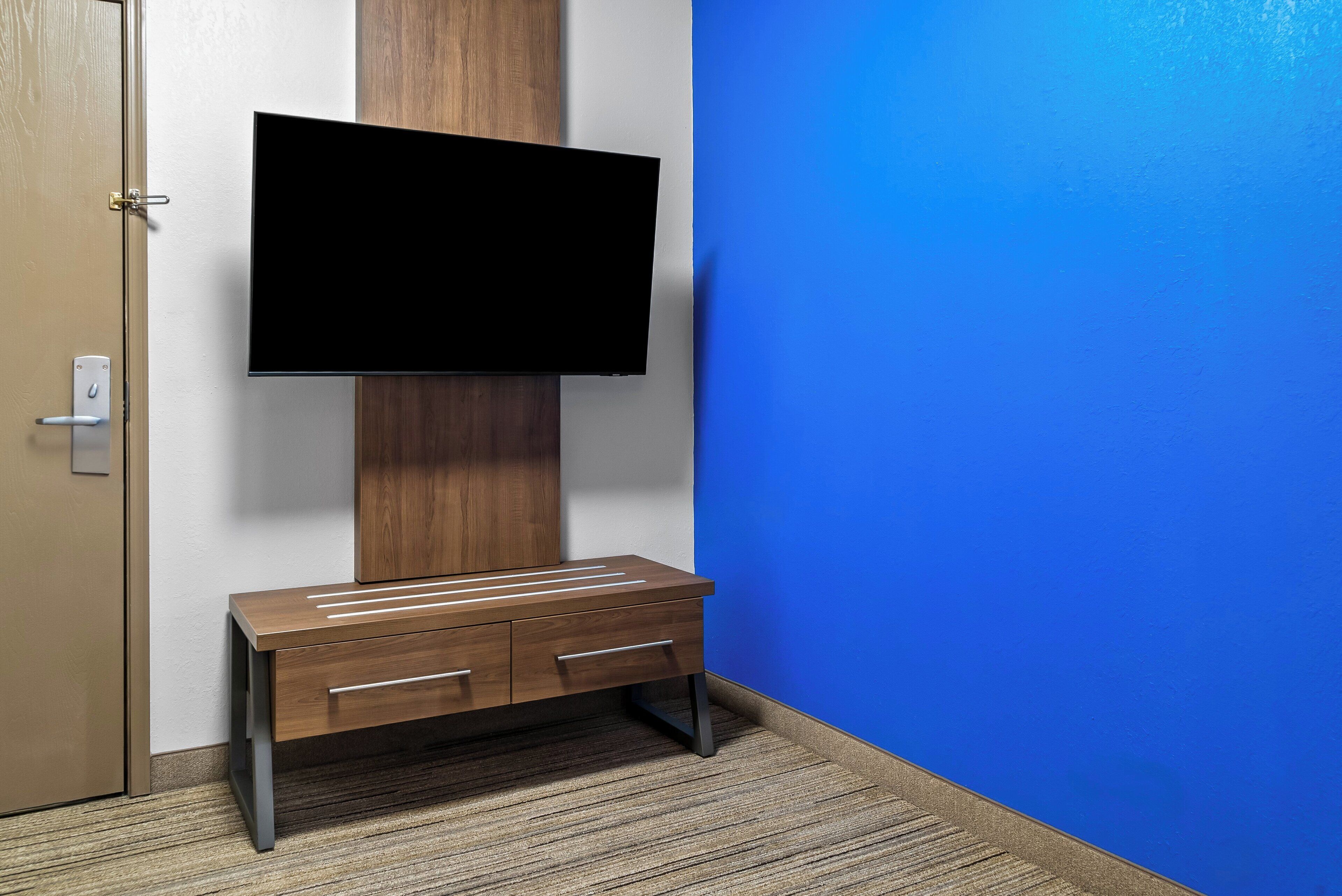Ein Zimmer mit einem an der Wand befestigten Flachbildfernseher, einer Holzkabine mit Schubladen und einer blauen Wand.
