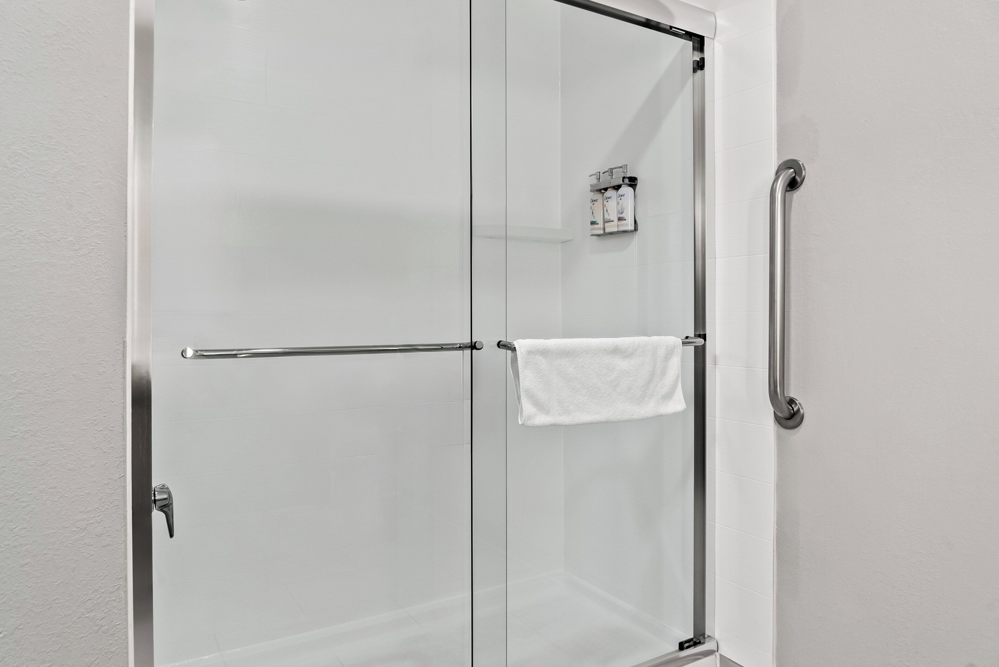 A glass-enclosed shower stall with a towel rack and a handrail.