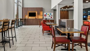 Ein modernes Café mit Holztischen und roten Stühlen, einem Flachbildfernseher und einer Wand mit bunten Tellern.