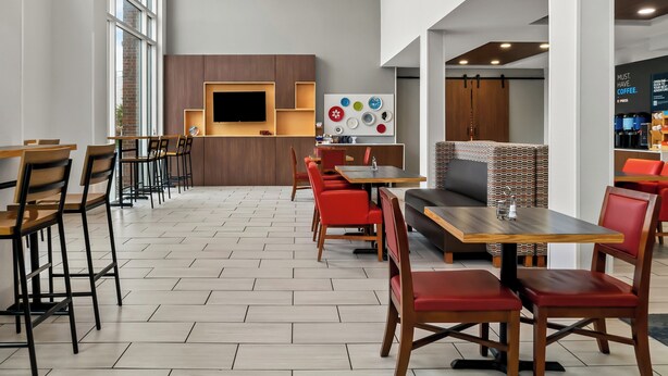 Een modern café met houten tafels en rode stoelen, een flatscreen televisie en een muur met kleurrijke borden.
