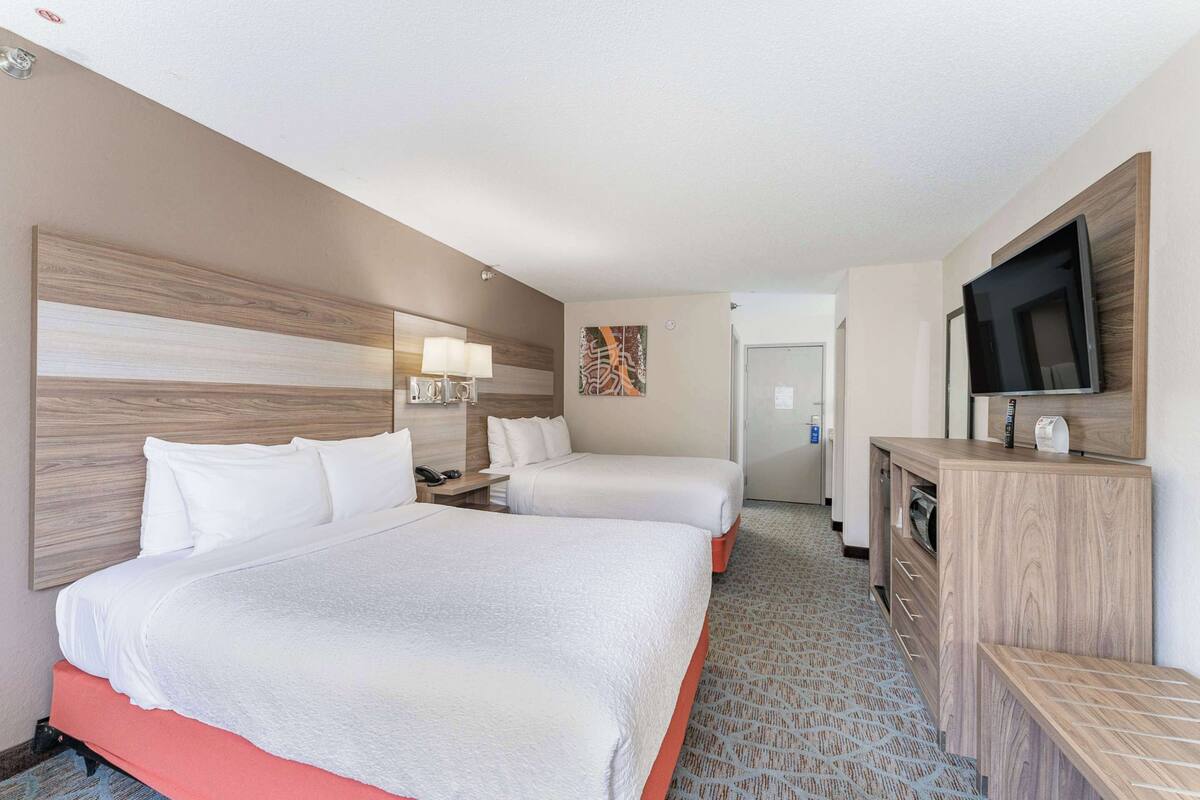 A hotel room with two beds, a desk, a television, and a painting on the wall.