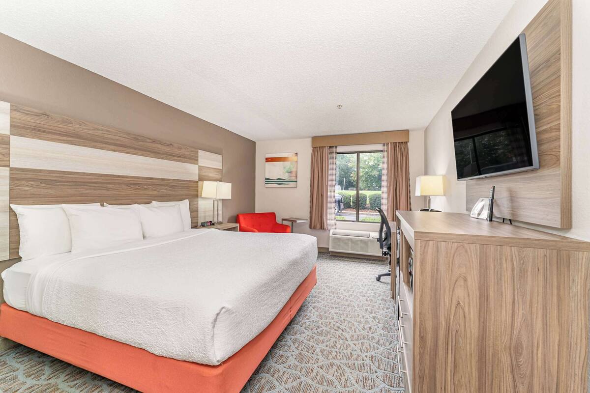 A hotel room with a large bed, a desk, a TV, and a window with curtains.