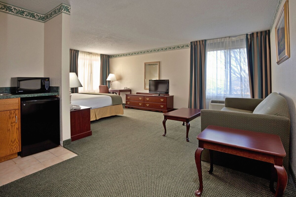 A hotel room with a bed, a desk, a television, a dresser, and a sofa.