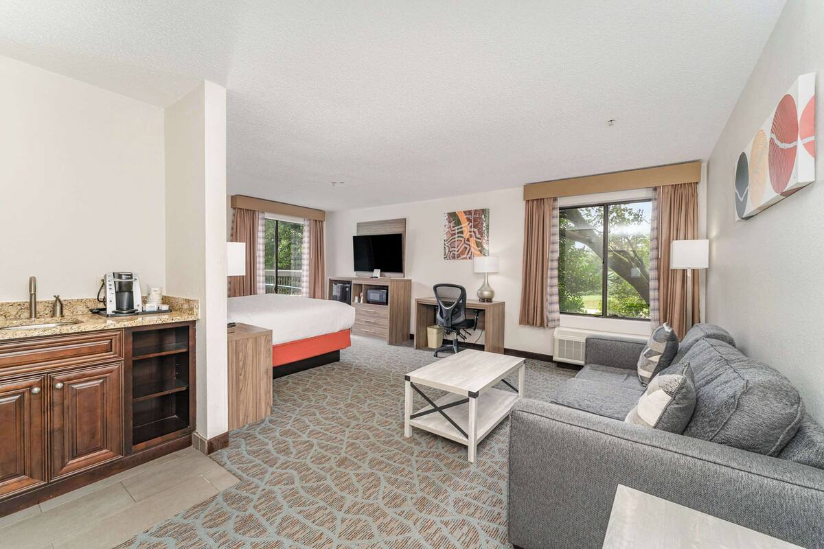 A hotel room with a bed, a desk, a sofa, a TV, and a window with curtains.