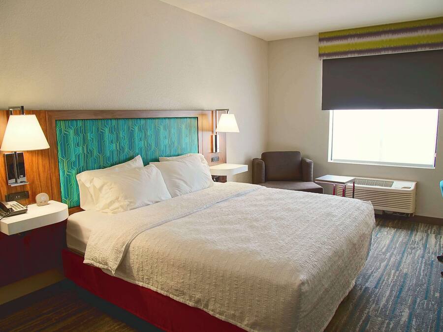 A hotel room with a large bed, two bedside tables with lamps, a chair, a desk, and a window with a view.