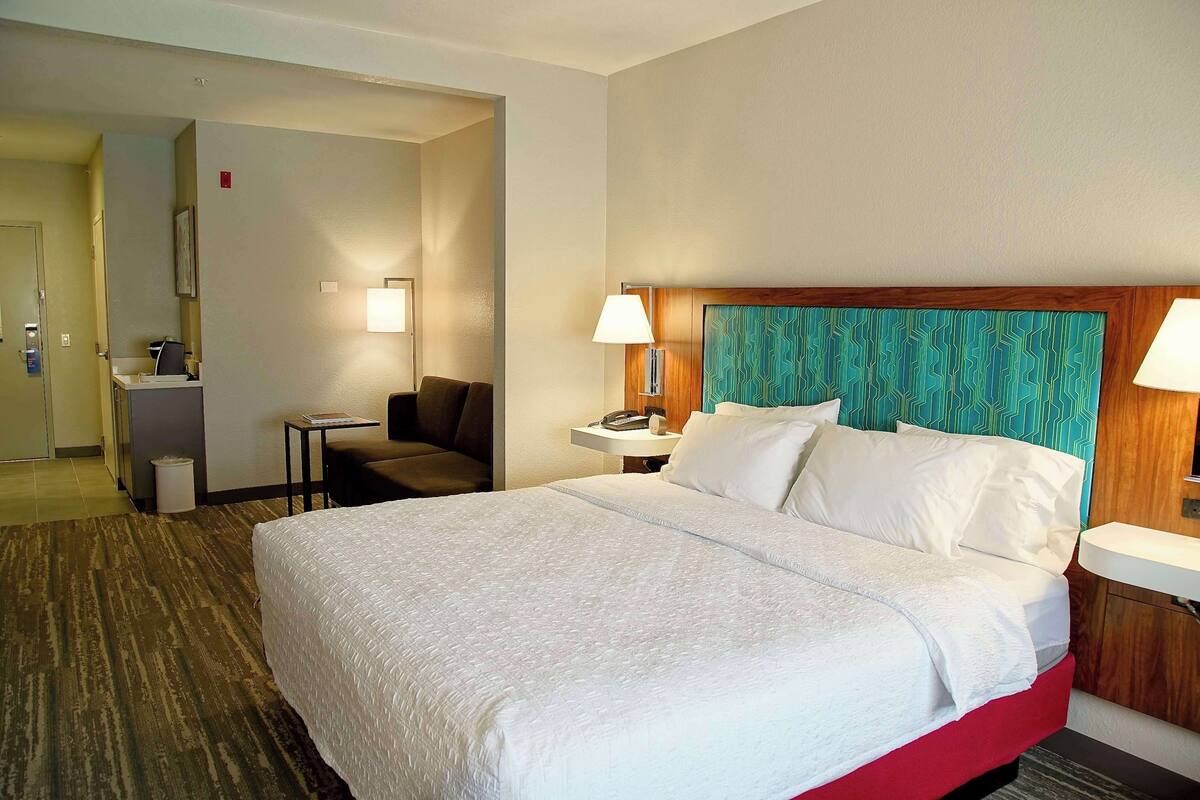 A hotel room with a large bed, a desk, a chair, a nightstand, and a bathroom.