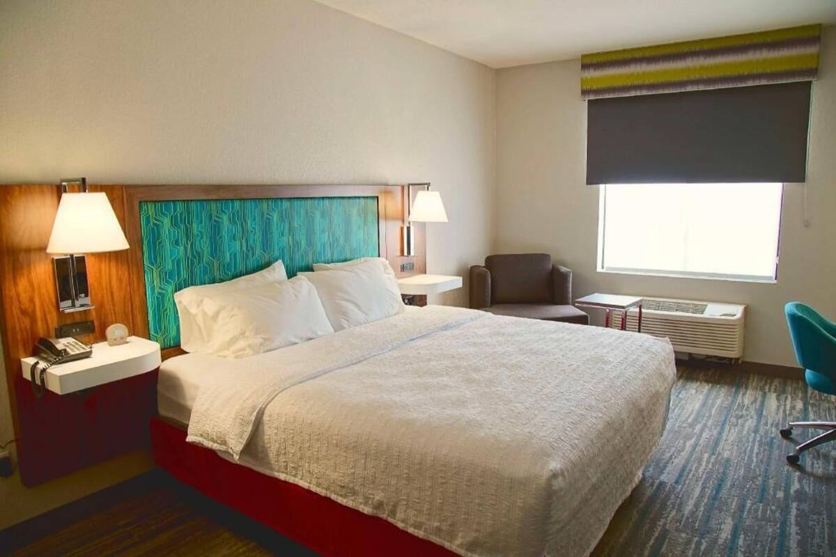 A hotel room with a bed, bedside tables, a chair, a window, and a radiator.