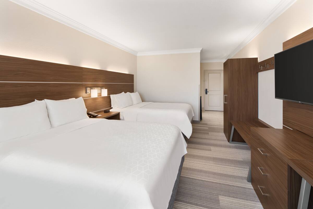 A hotel room with two beds, a TV, wooden headboard, and a walk-in closet.