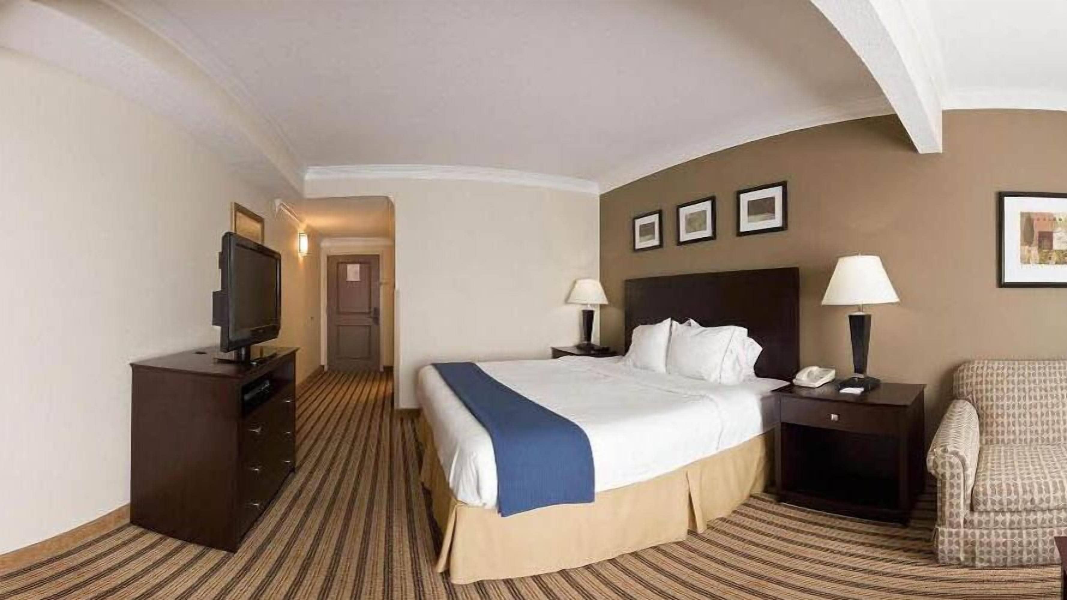 Une chambre d’hôtel comprenant un lit, une télévision, un bureau avec une lampe, une chaise et une porte donnant sur une autre pièce.