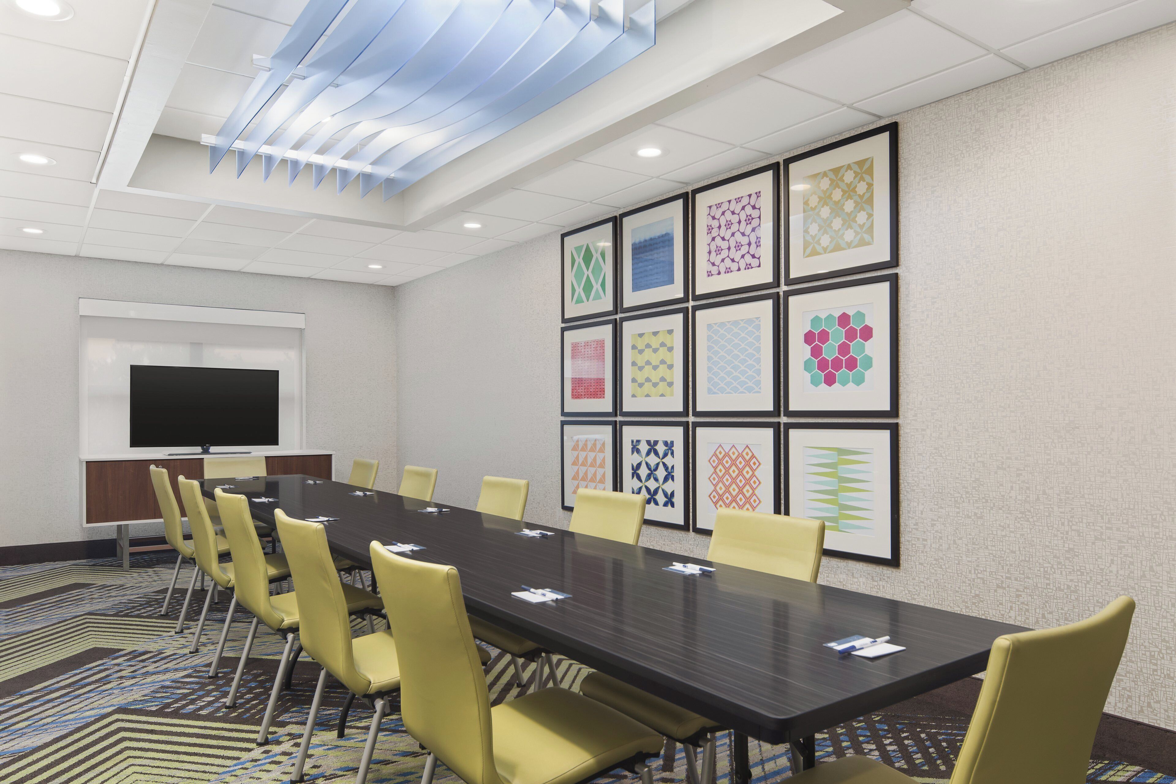 A conference room with a long table, yellow chairs, and framed geometric patterns on the wall.