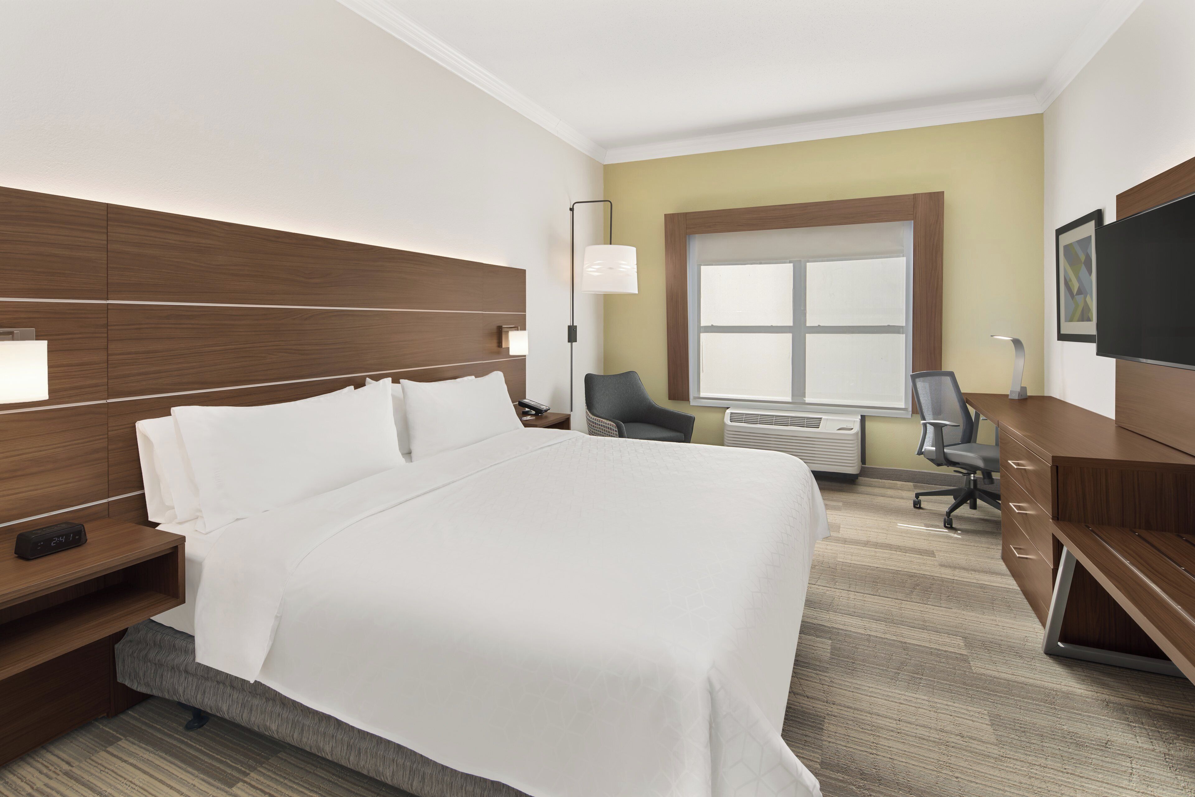 A hotel room with a large bed, a desk, a chair, a TV, and a window.