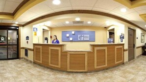 A hotel reception area with a curved reception desk, two receptionists, a blue sign with 'H' and 'Express', and a tiled floor. - Holiday Inn Express & Suites Byron by IHG (Byron)