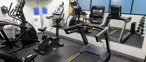 A gym with treadmills, elliptical machines, and a bench.
