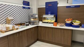 A breakfast bar with bakery and fruit options, a sign for 'EGG-XACTLY', and a 'TREAT YOURSELF' sign.