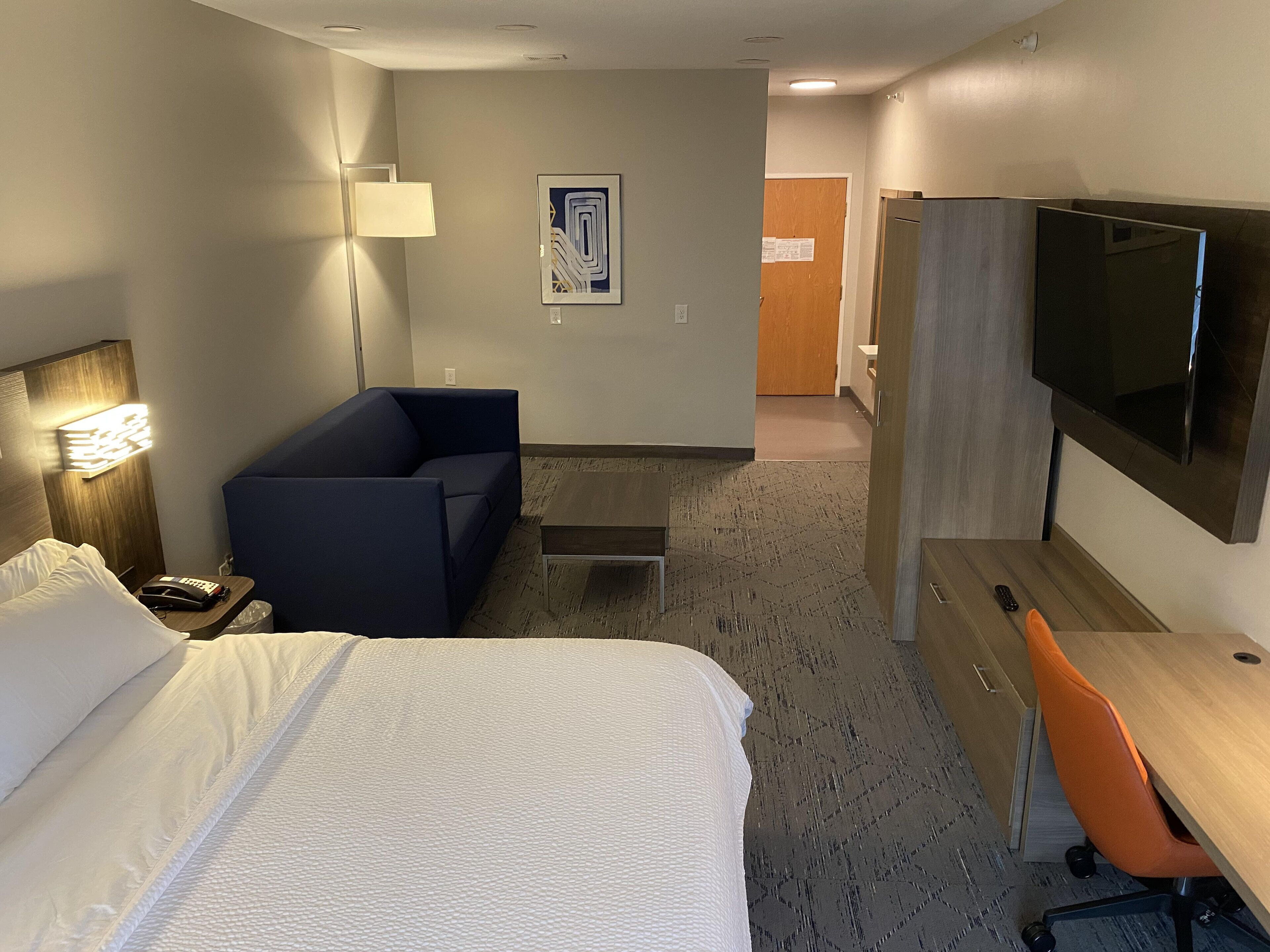 Una habitación de hotel con cama, escritorio, silla, sofá, televisor y lámpara.