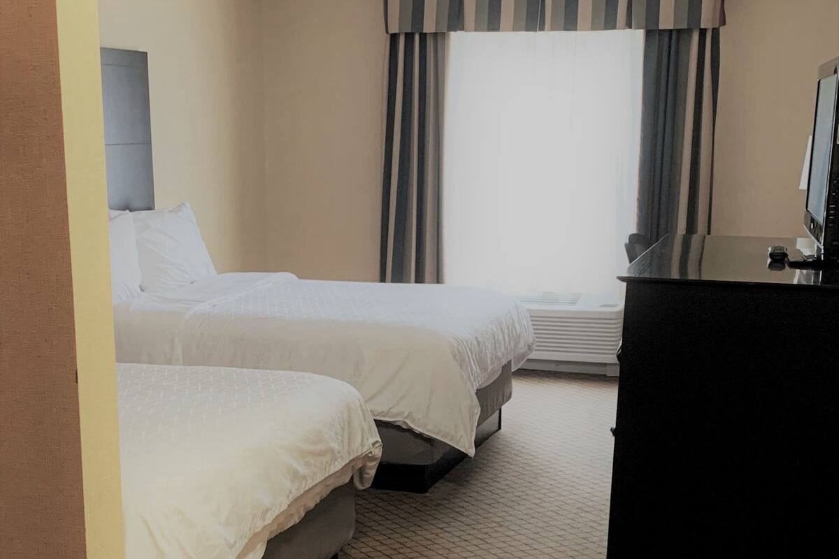 Une chambre d’hôtel avec deux lits, un bureau et une fenêtre avec des rideaux.