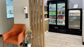 A seating area with a modern orange chair, a decorative plant, and a beverage vending machine with a freezer section.
