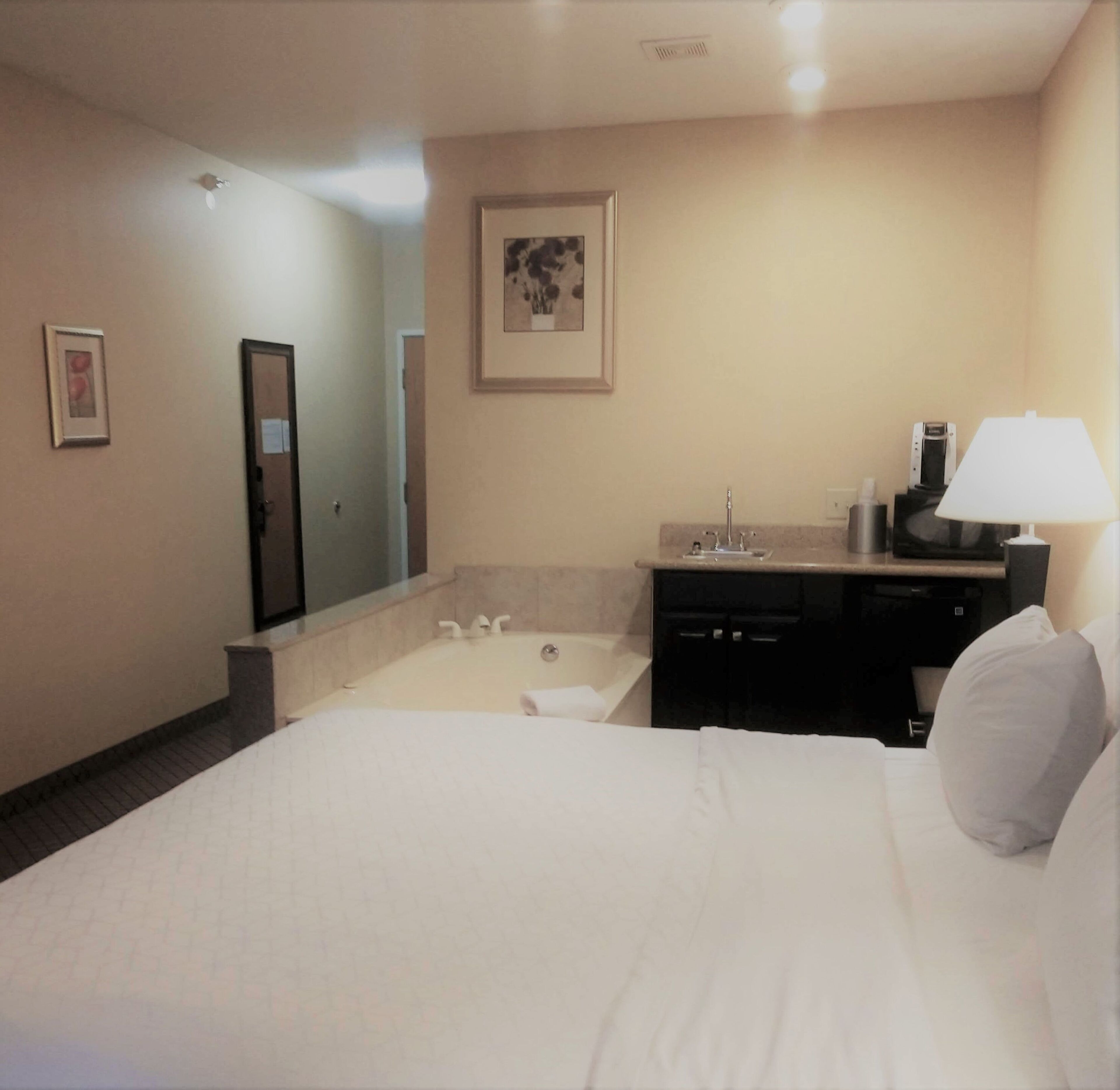 Ein Hotelzimmer mit einem großen Bett, einem Badezimmer mit Badewanne, Waschbecken und Spiegel.