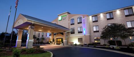 A Holiday Inn Express & Suites building with a covered entrance, multiple windows, and a flagpole.