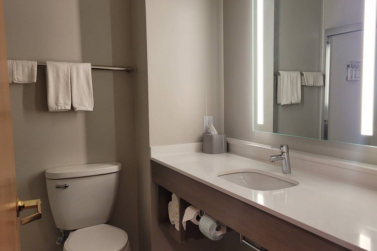 Une salle de bain moderne avec des toilettes, un lavabo et un miroir. Des serviettes sont suspendues sur un porte-serviettes placé au-dessus des toilettes.