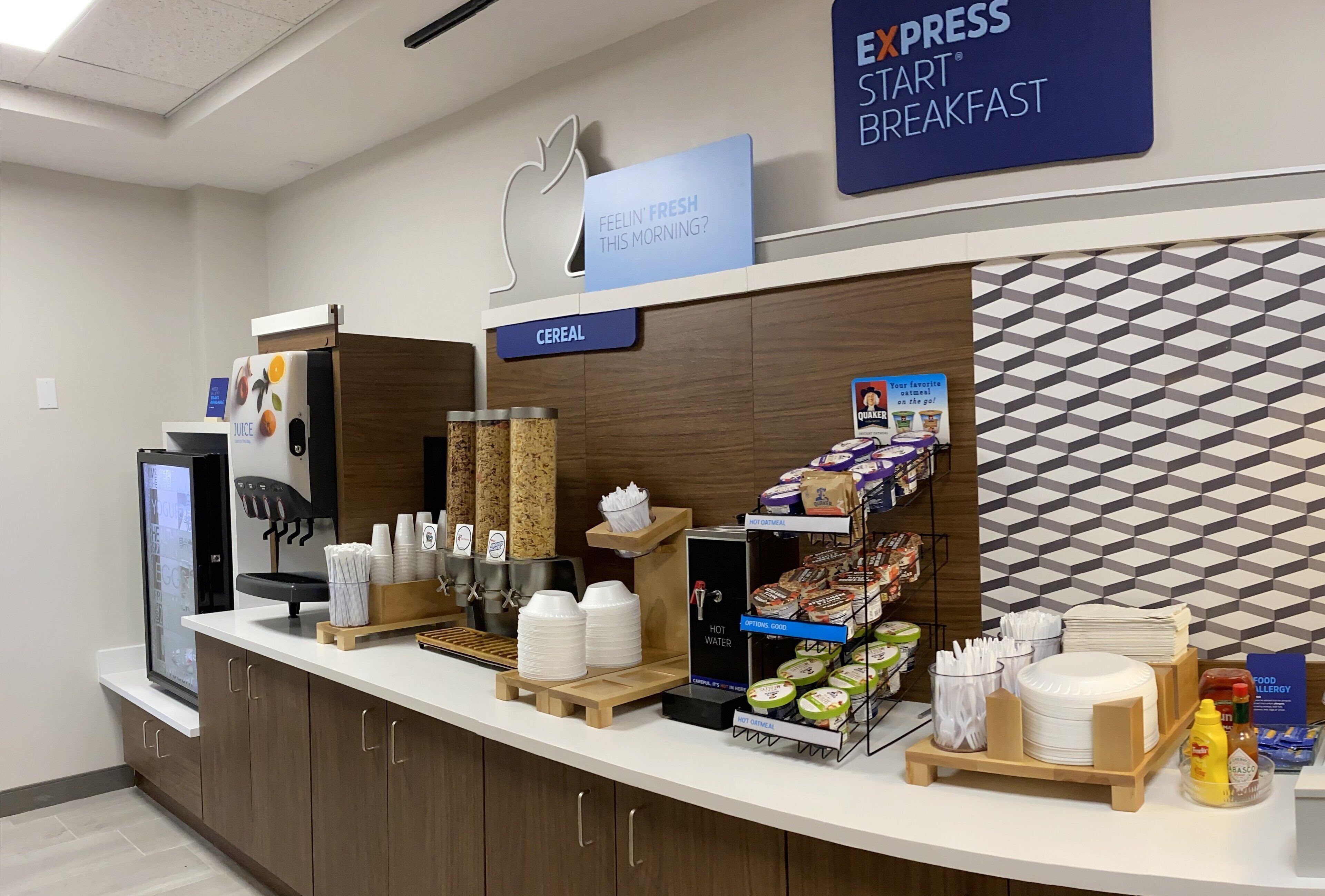 A breakfast area with a sign reading "Express Start Breakfast," a juice dispenser, cereal, and a variety of food items.
