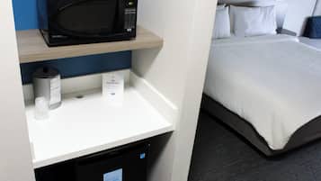 Ein Hotelzimmer mit Mikrowelle auf einem Regal, einem kleinen Mülleimer und einem Bett mit weißer Bettwäsche.