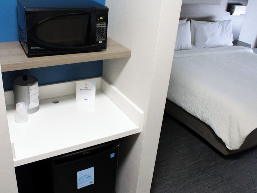 Ein Hotelzimmer mit Mikrowelle auf einem Regal, einem kleinen Mülleimer und einem Bett mit weißer Bettwäsche.