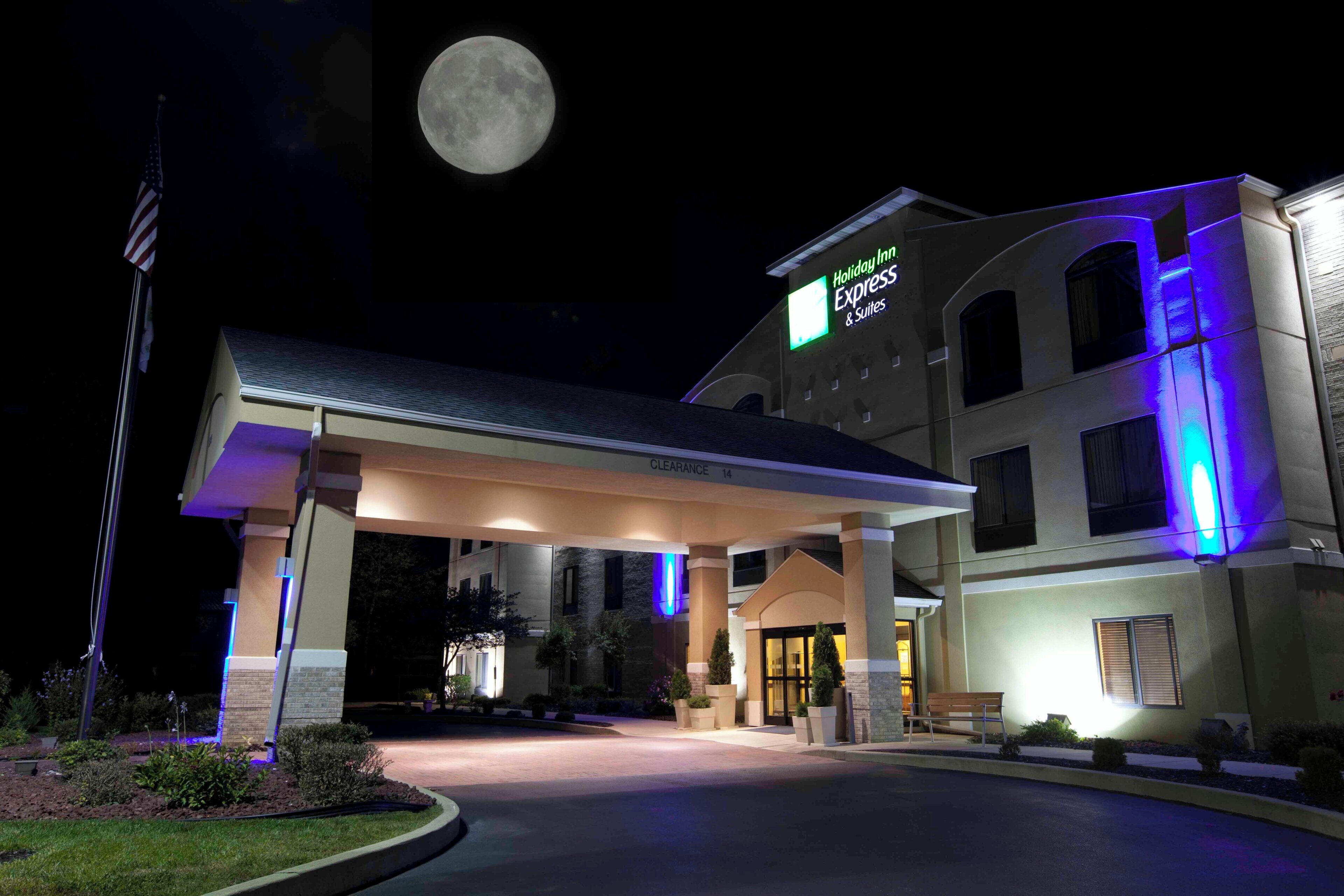 A Holiday Inn Express & Suites hotel with a covered entrance, a flag, and a full moon in the background.