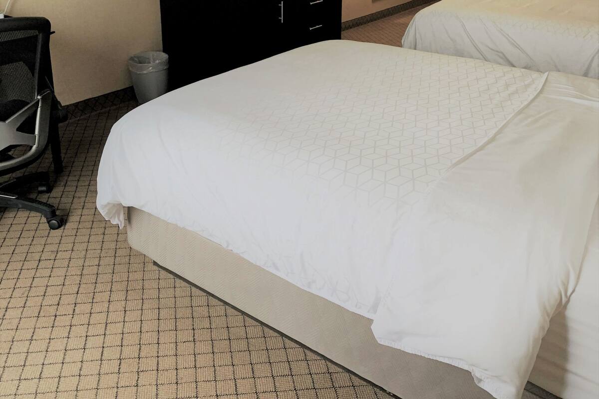 Une chambre d’hôtel avec deux lits, un bureau avec un ordinateur, une télévision et une poubelle.