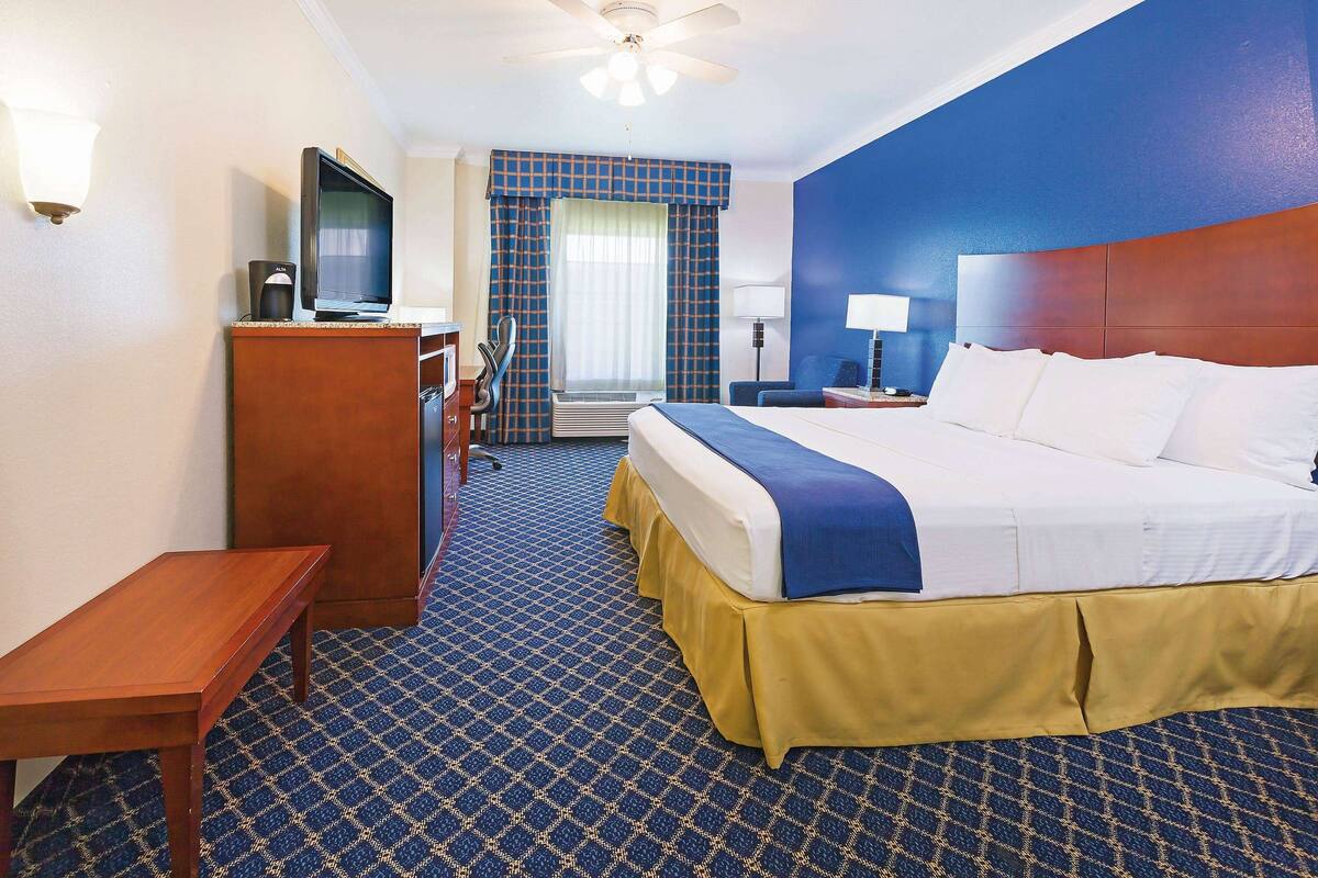 A hotel room with a bed, a desk, a television, and a window with curtains.