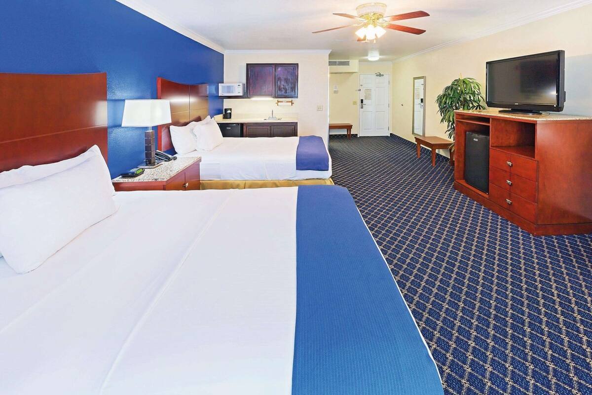 A hotel room with two beds, a desk, a television, and a ceiling fan.