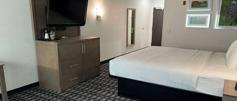 A hotel room with a bed, a television, a dresser, and a mirror.