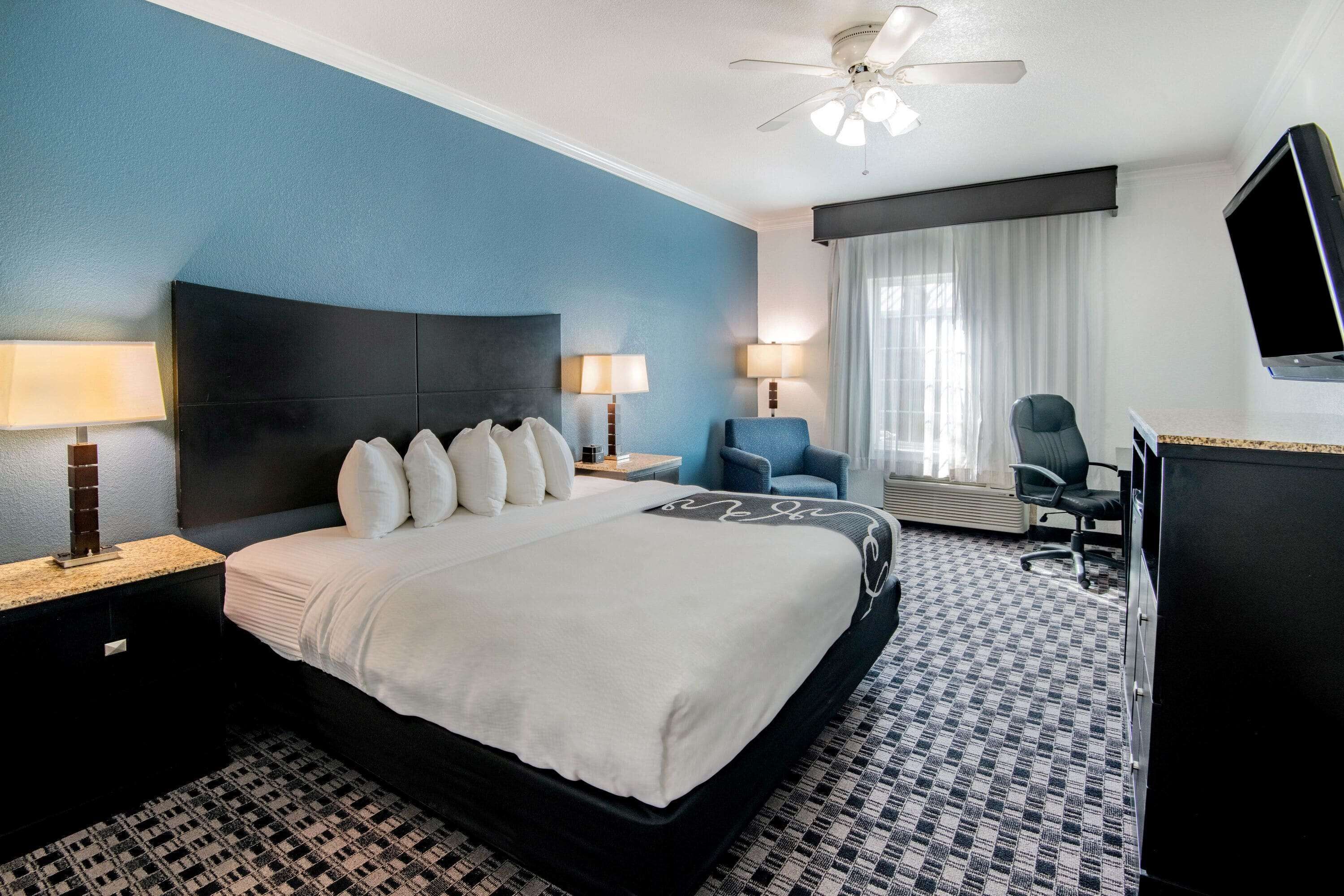 A hotel room with a large bed, two bedside tables with lamps, a chair, a desk, and a TV.