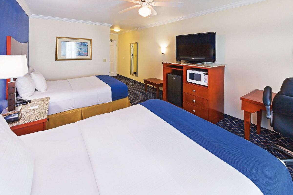 A hotel room with two beds, a television, a desk, and a refrigerator.