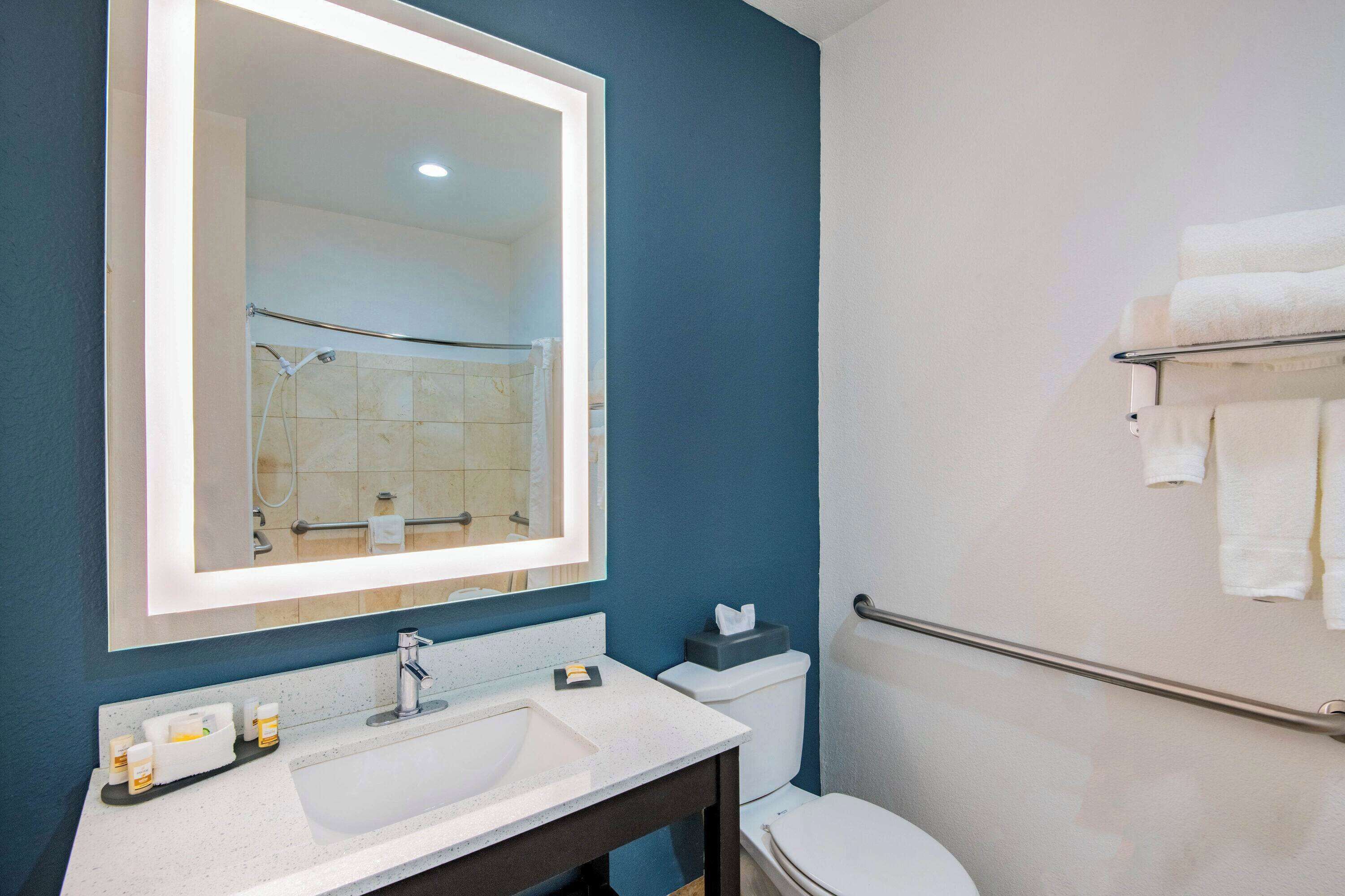 Un baño con lavamanos blanco, un espejo, toallero y retrete.