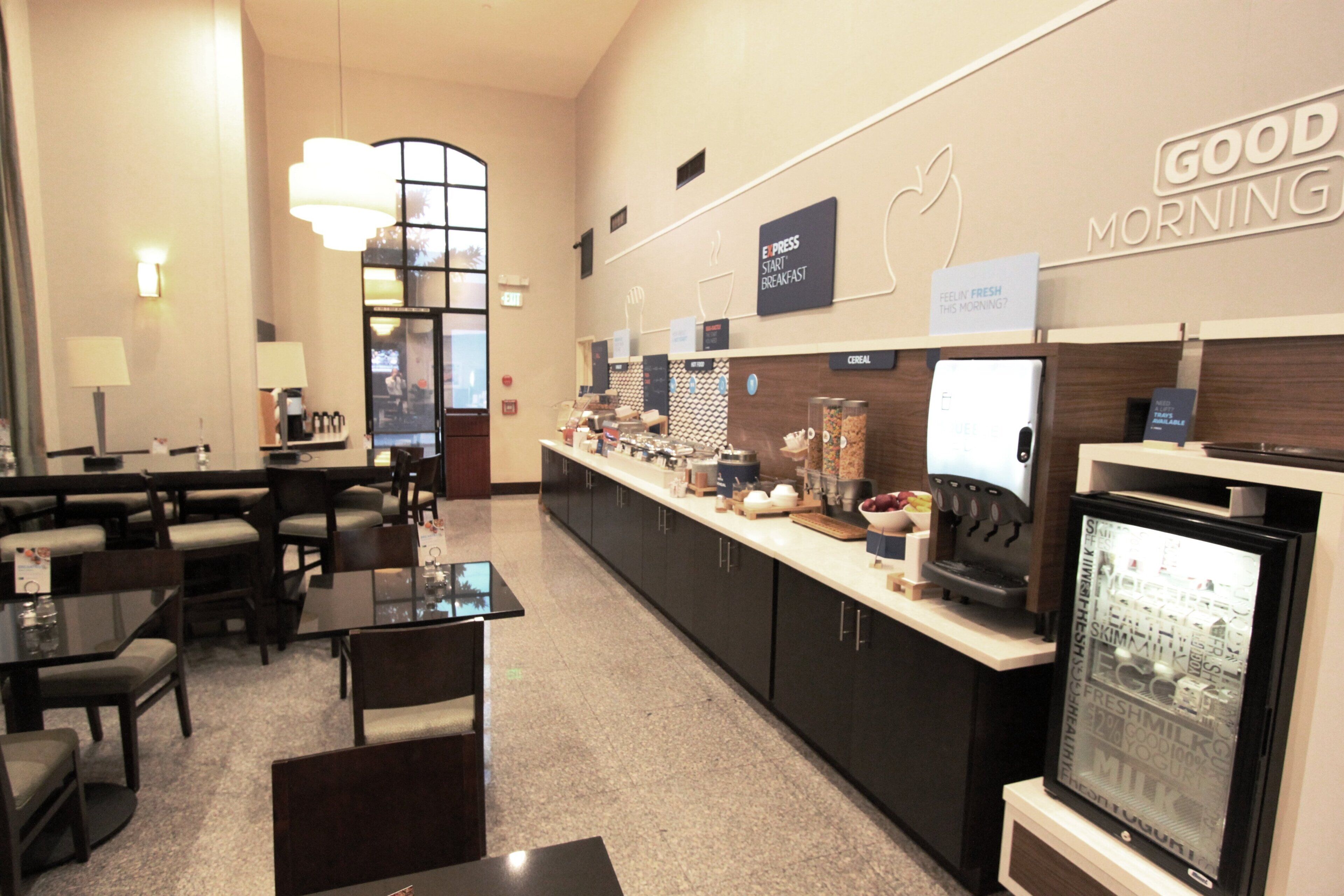 A hotel breakfast area with a counter, seating, and a refrigerator.