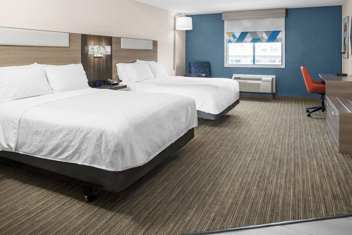 A hotel room with two beds, a desk, a chair, a lamp, and a window with a view.