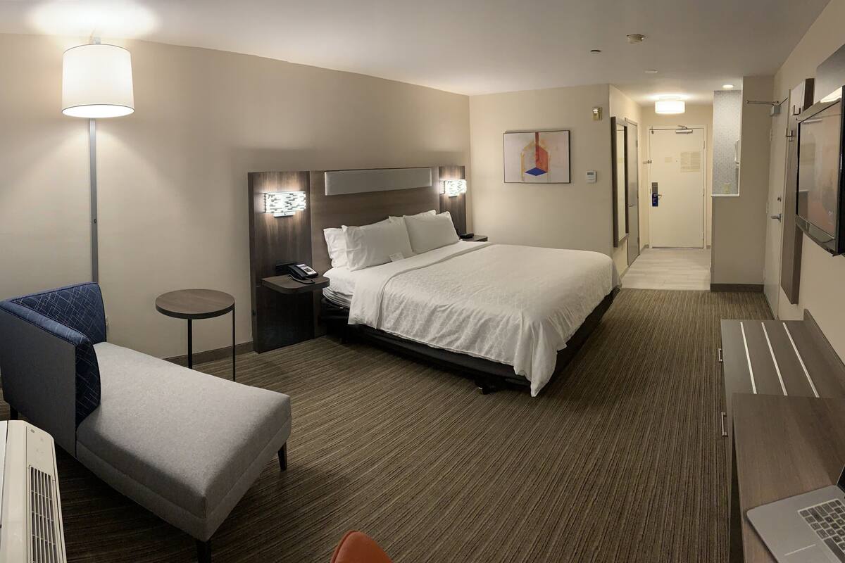 A hotel room with a bed, a desk, a chair, a lamp, and a TV.